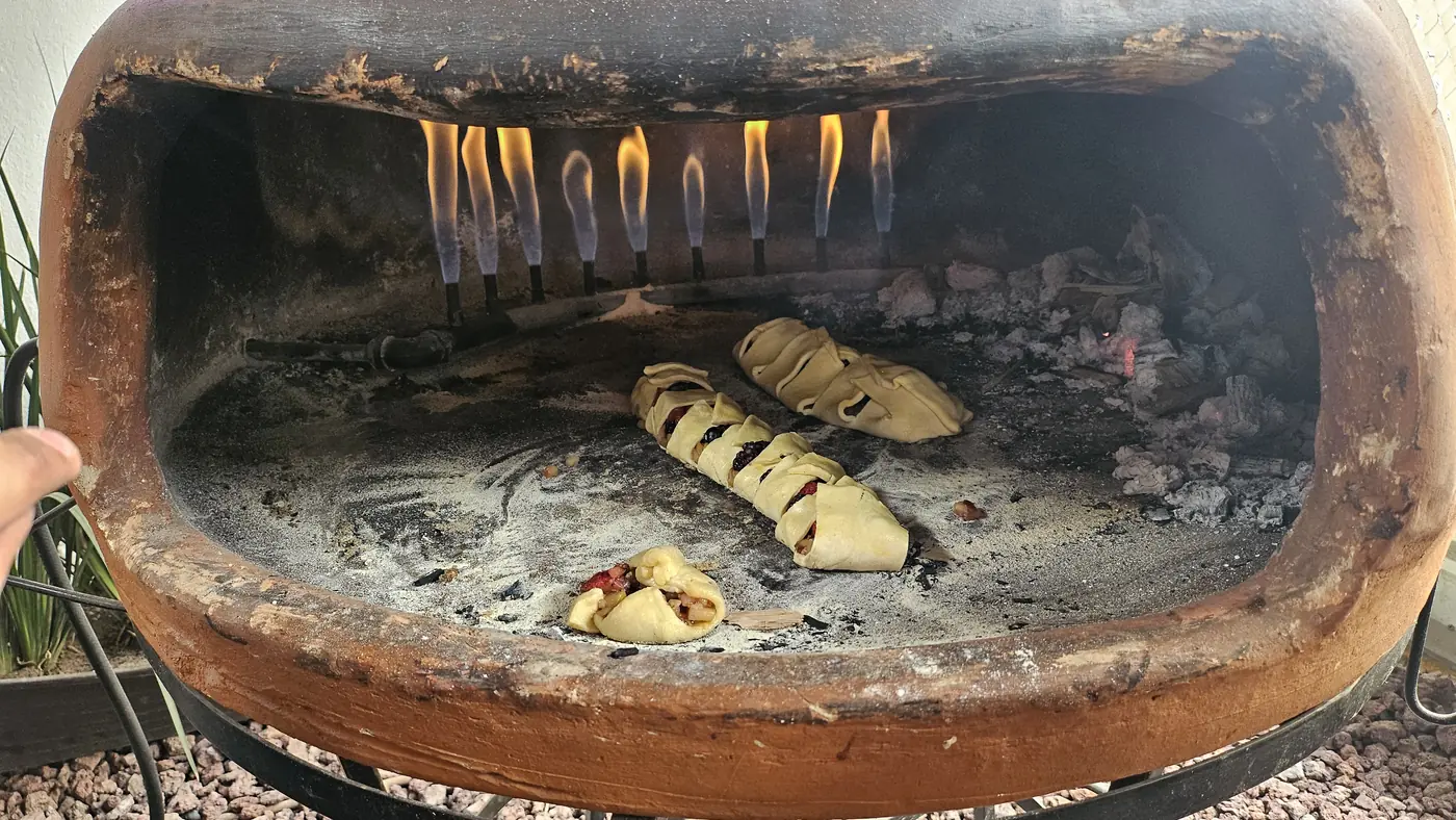 Interior del horno de barro con llamas vivas y pan trenzado horneándose