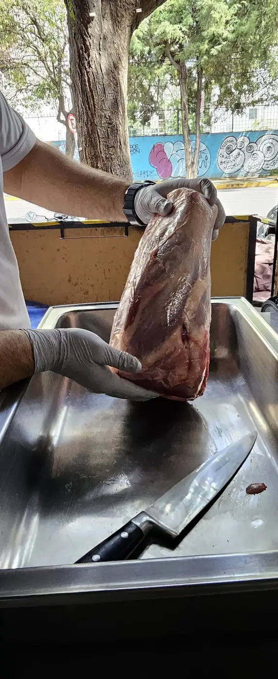 Manos con guante limpiando una pieza de res sobre la mesa de trabajo de la carnicería