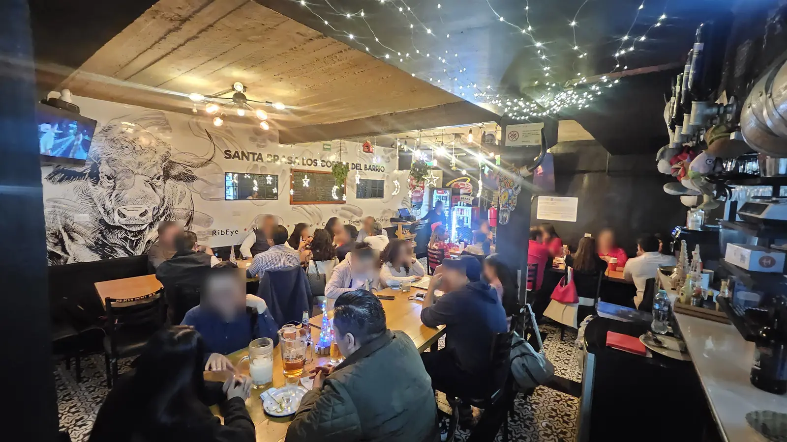El salón lleno de noche, con series de luces y el mural del toro al fondo